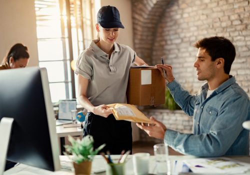 smiling-female-courier-delivering-package-businessman-while-he-is-working-office
