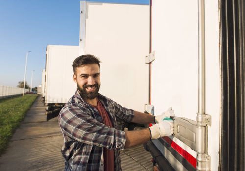 smiling-truck-driver-working-gloves-opening-closing-truck-trailer-back-doors-checking-goods-transportation